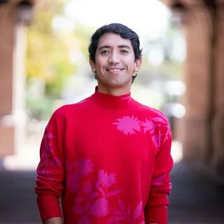 Smiling man wearing a bright red sweater with pink floral patterns, standing outdoors.